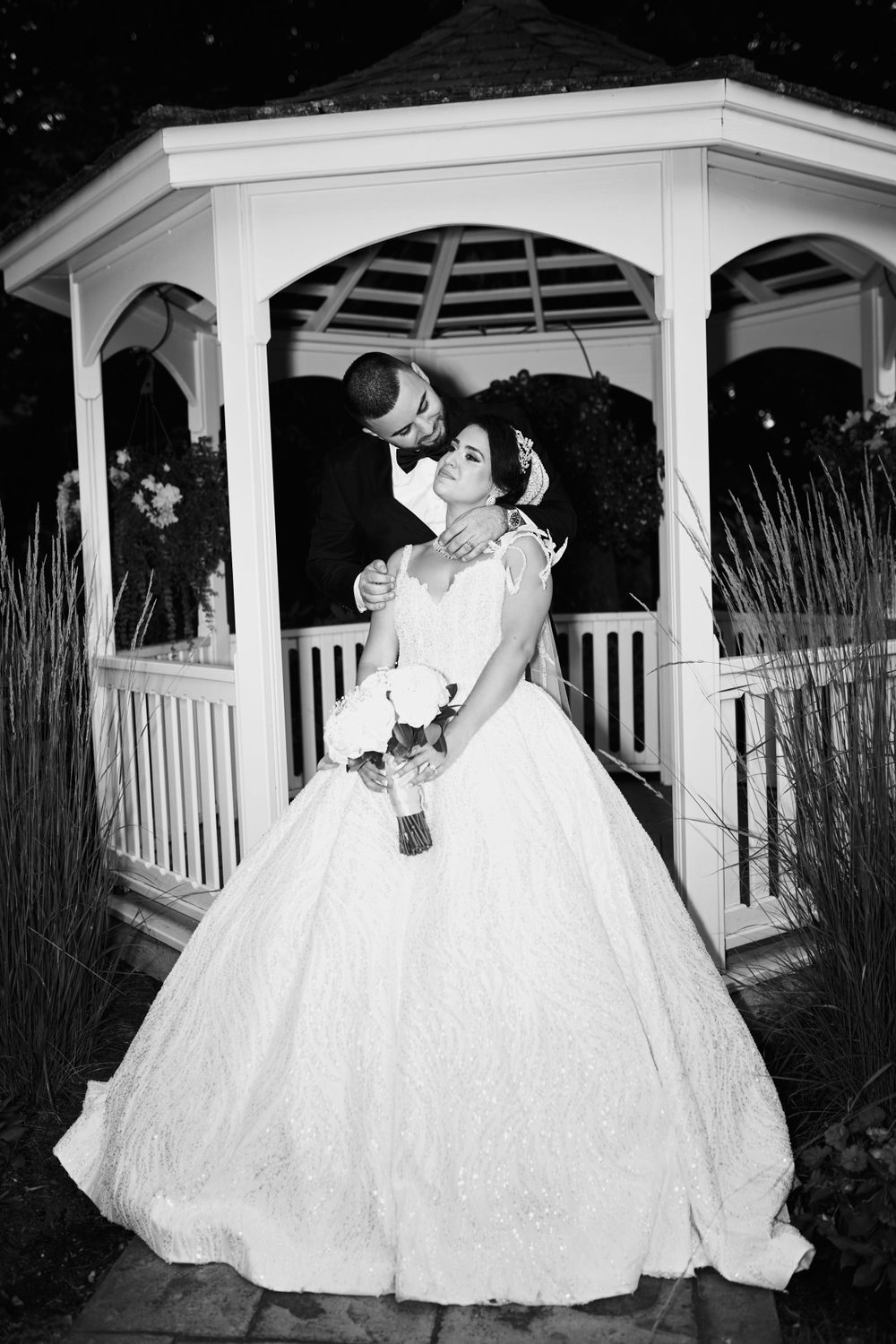 A dramatic black and white wedding portrait in a white gazebo at night.