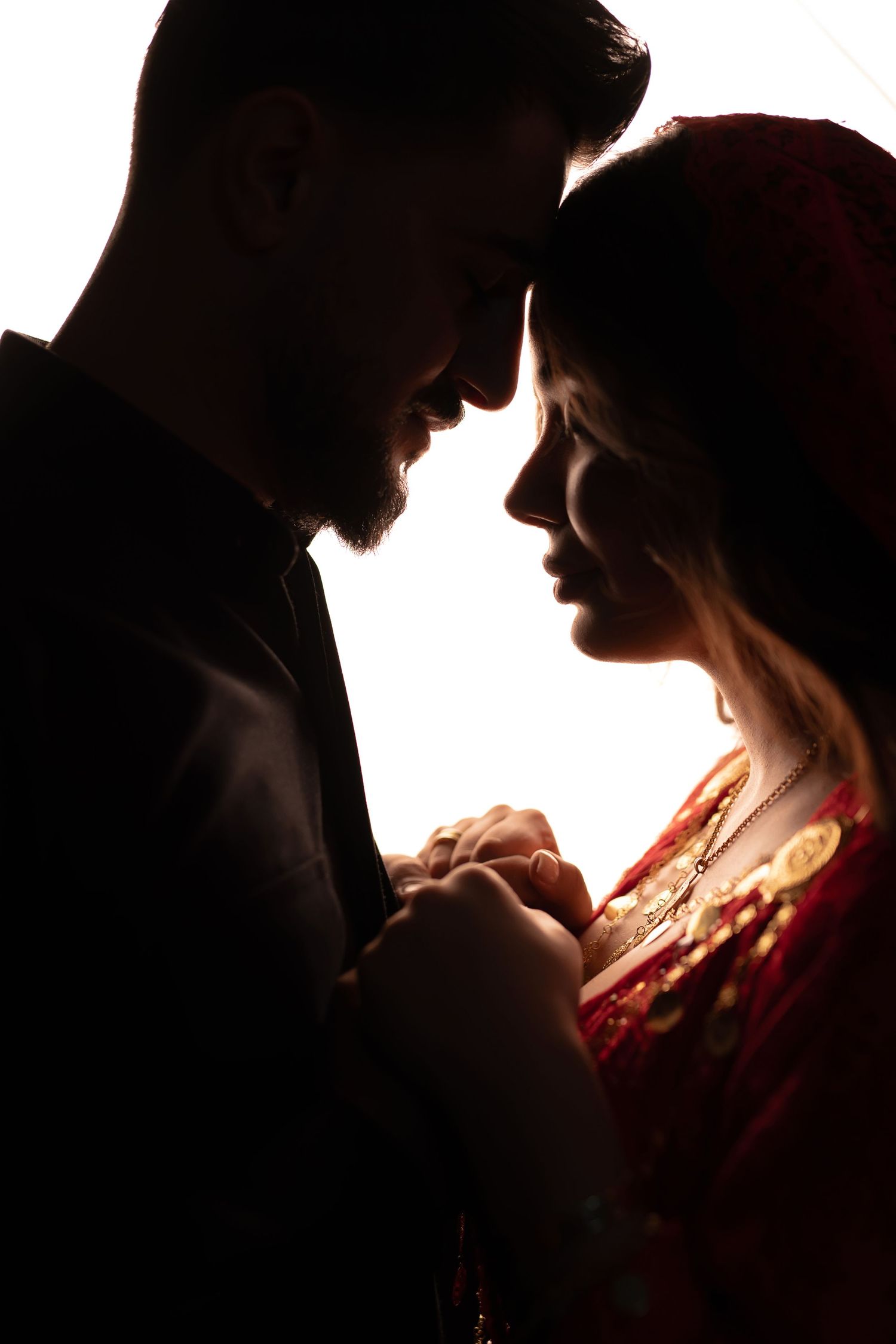 Silhouetted couple in intimate moment against bright background, holding hands while standing close together.