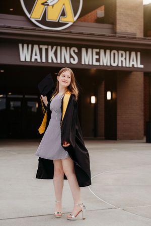 A woman in a black blazer and grey dress poses near the Watkins Memorial building entrance.