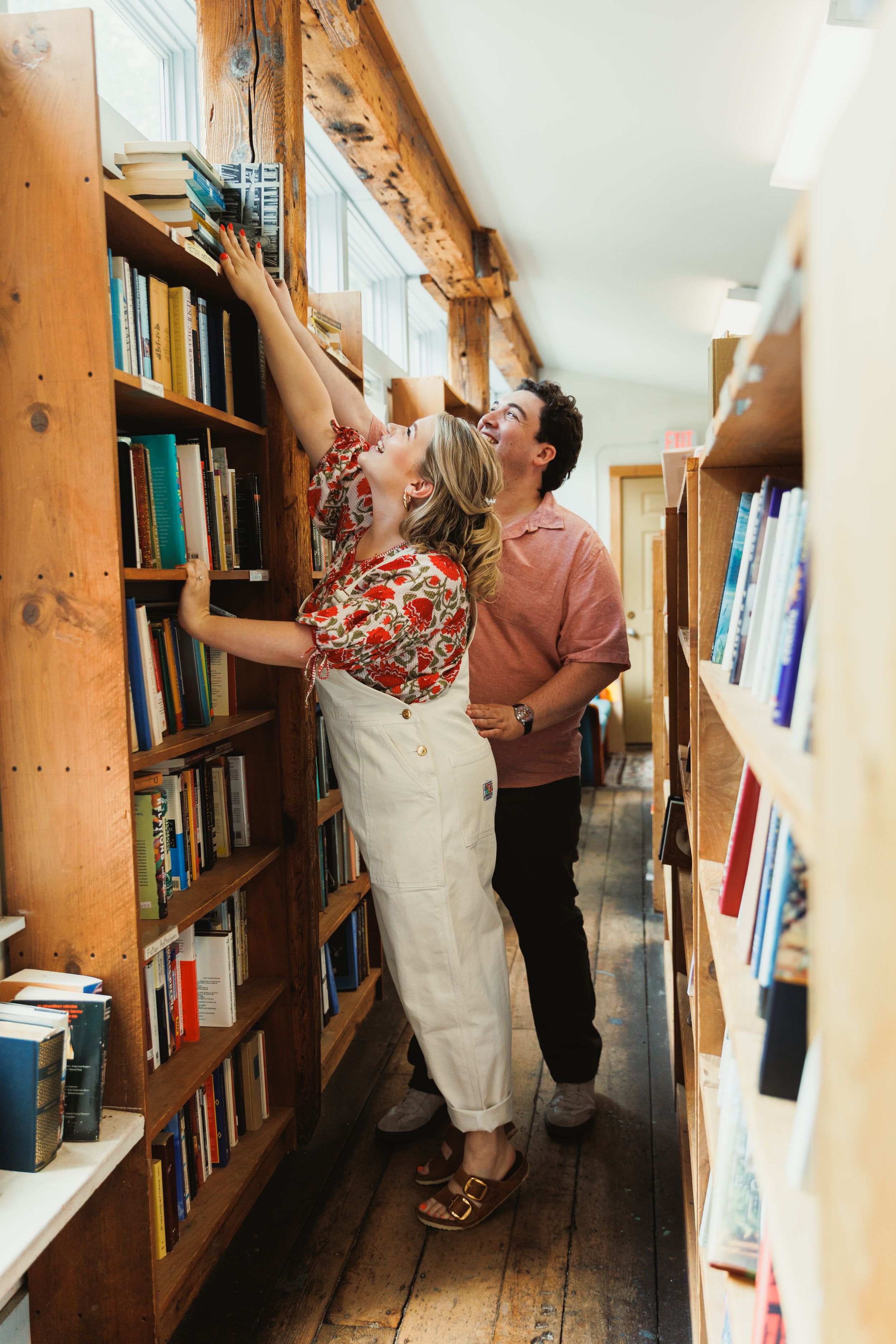 Couple browsing books together in a cozy library aisle with wooden shelves and natural lighting.