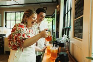 Two people in a restaurant looking at a mobile phone while standing near colorful cocktail drinks.