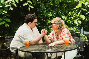 A couple shares a romantic moment at an outdoor patio table with orange drinks on a sunny day.