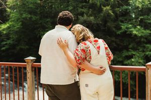 Couple embracing while looking out over scenic deck railing surrounded by green trees.