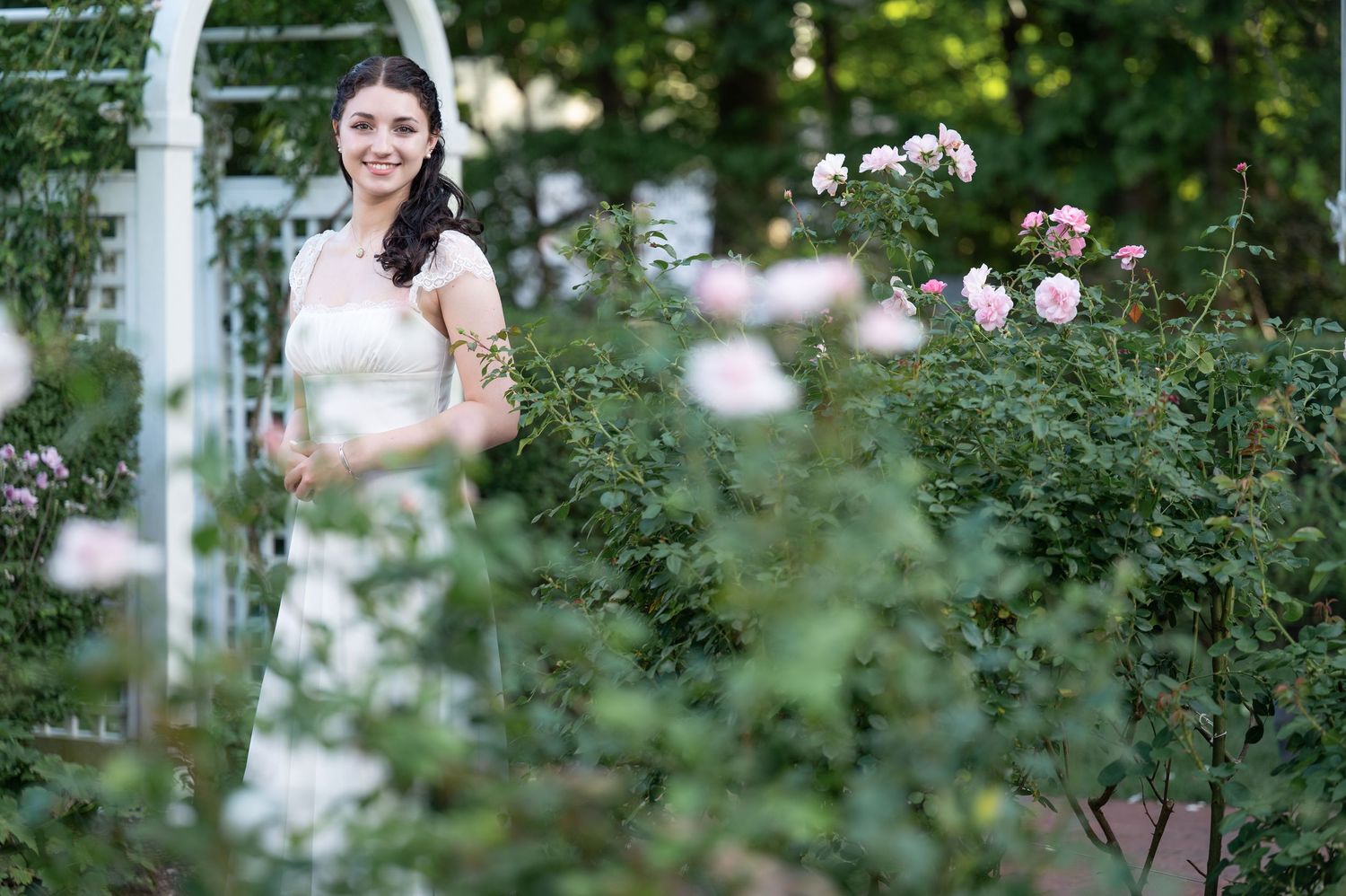 Someone in a white lace dress poses gracefully in a sunny meadow filled with yellow wildflowers and greenery.