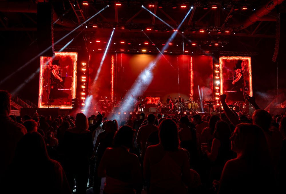 Crowd silhouetted against dramatic red stage lighting at a live music concert venue.