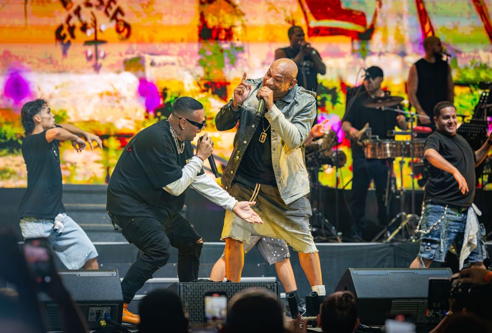 Two male performers energetically rap together on a colorful graffiti-style concert stage.