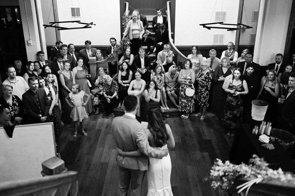 Wedding guests gather on a dance floor during a reception celebration as they watch the festivities.