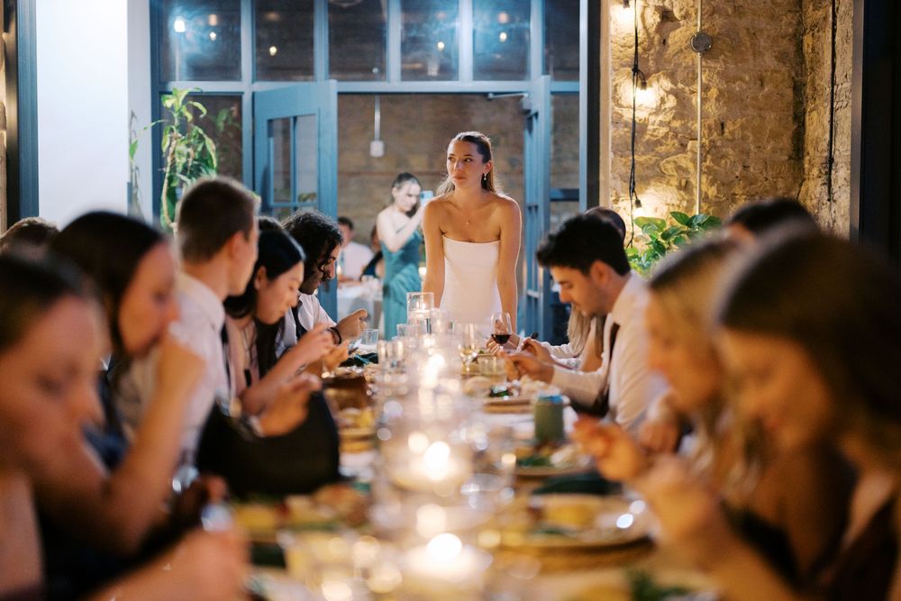 Candlelit dinner gathering with guests seated at a long table in an intimate restaurant setting.