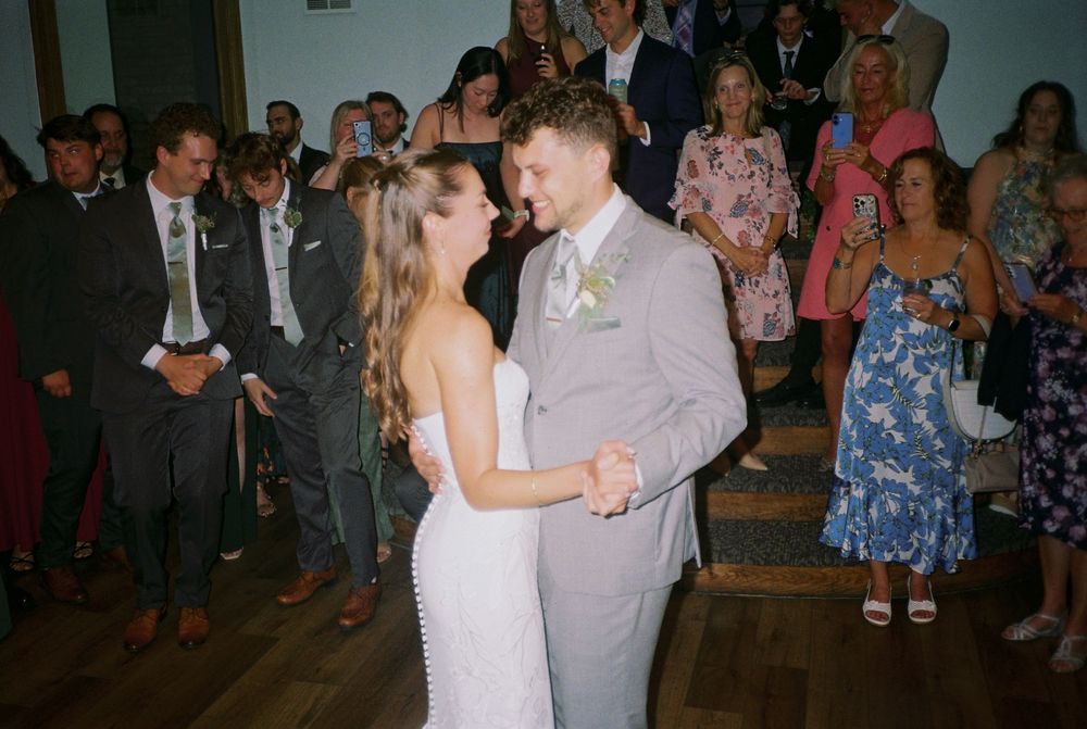 A couple shares a romantic dance at their wedding reception while guests look on from the background.