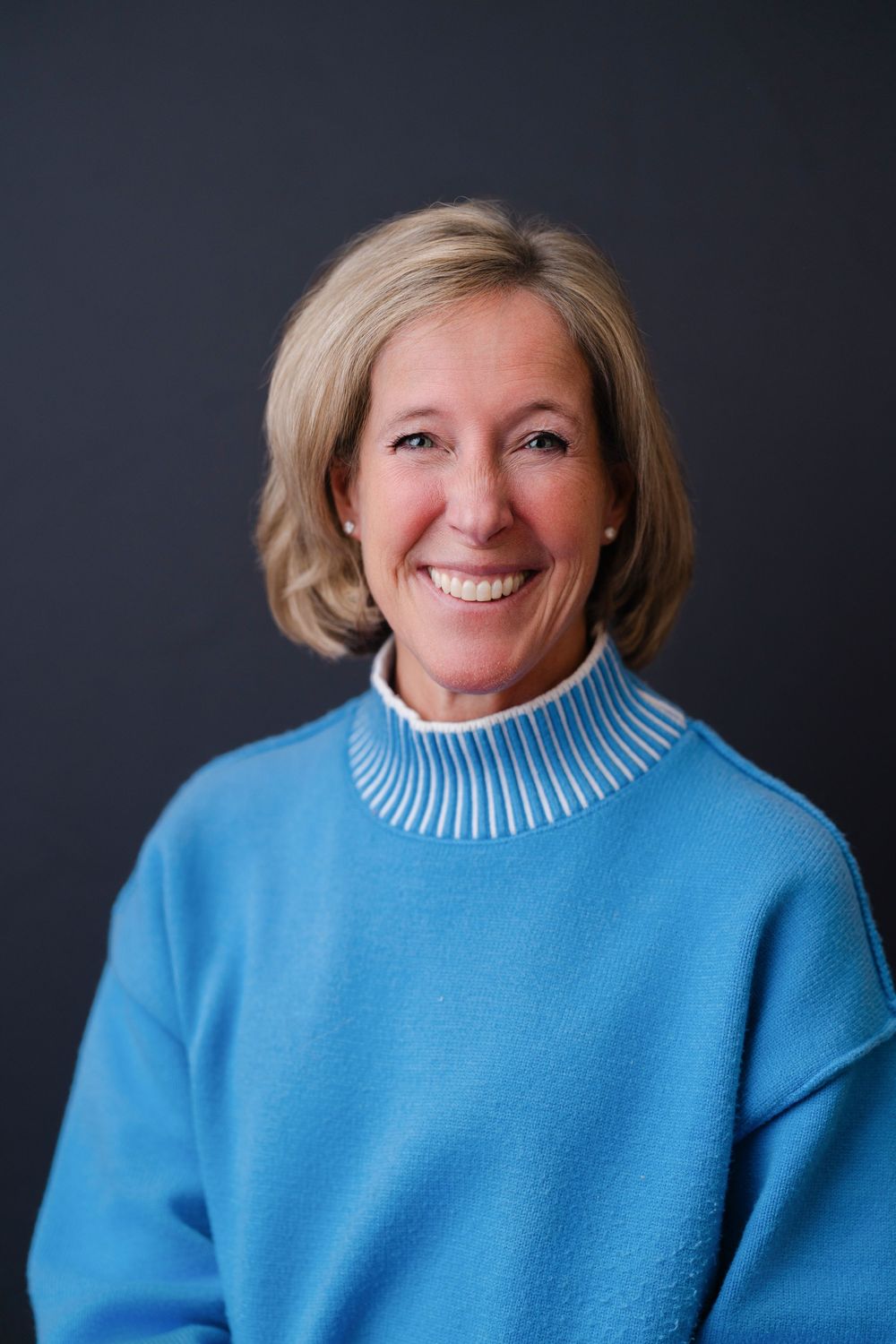 Professional studio portrait series showing warm expressions against dark background wearing bright blue sweater.