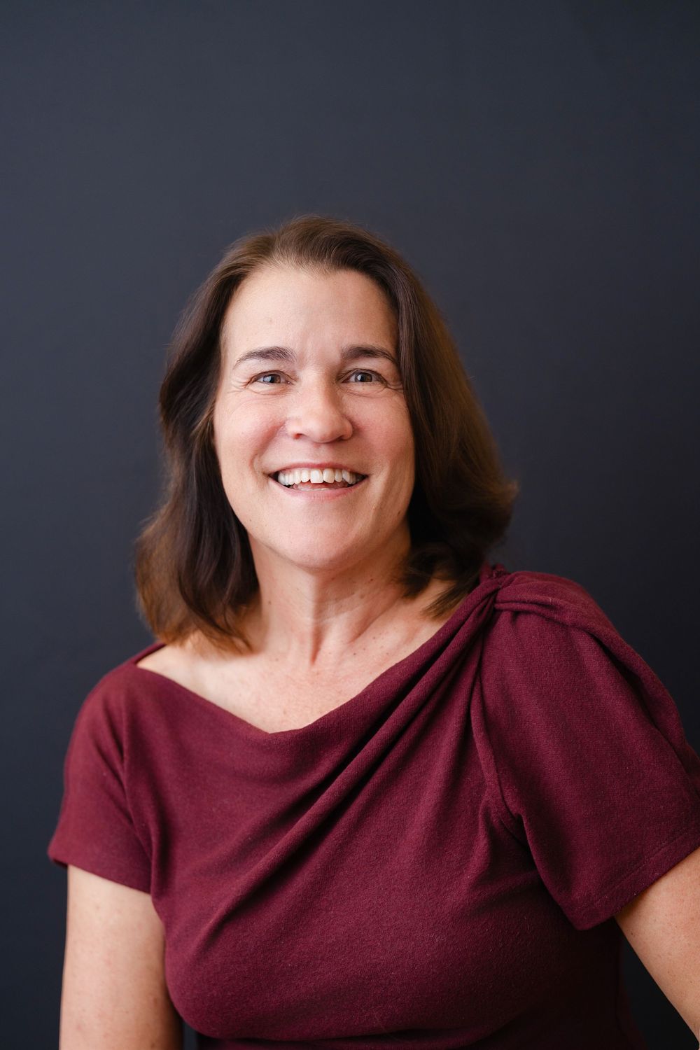 A series of four headshots showing someone wearing a burgundy top against a dark background, expressing joy and warmth.