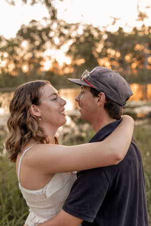 Couple embracing and smiling at each other during golden hour sunset near a lake.