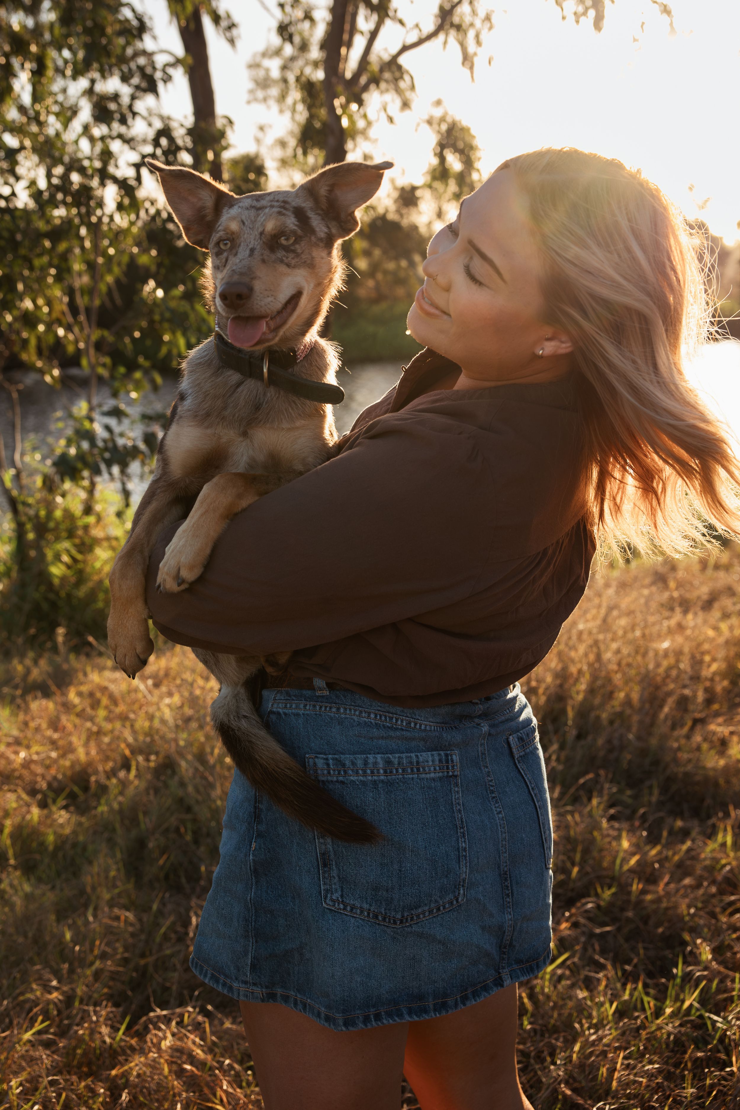 Young woman in denim skirt holds her happy brown dog outdoors at golden hour sunsetRockhampton Queensland