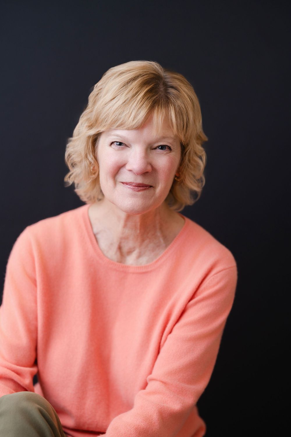 Warm portrait of person in coral sweater smiling against dark background.