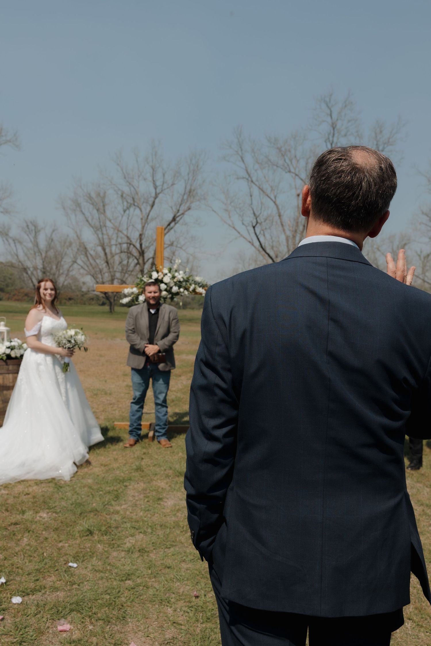 Outdoor wedding ceremony setup with guests gathering on grassy field.