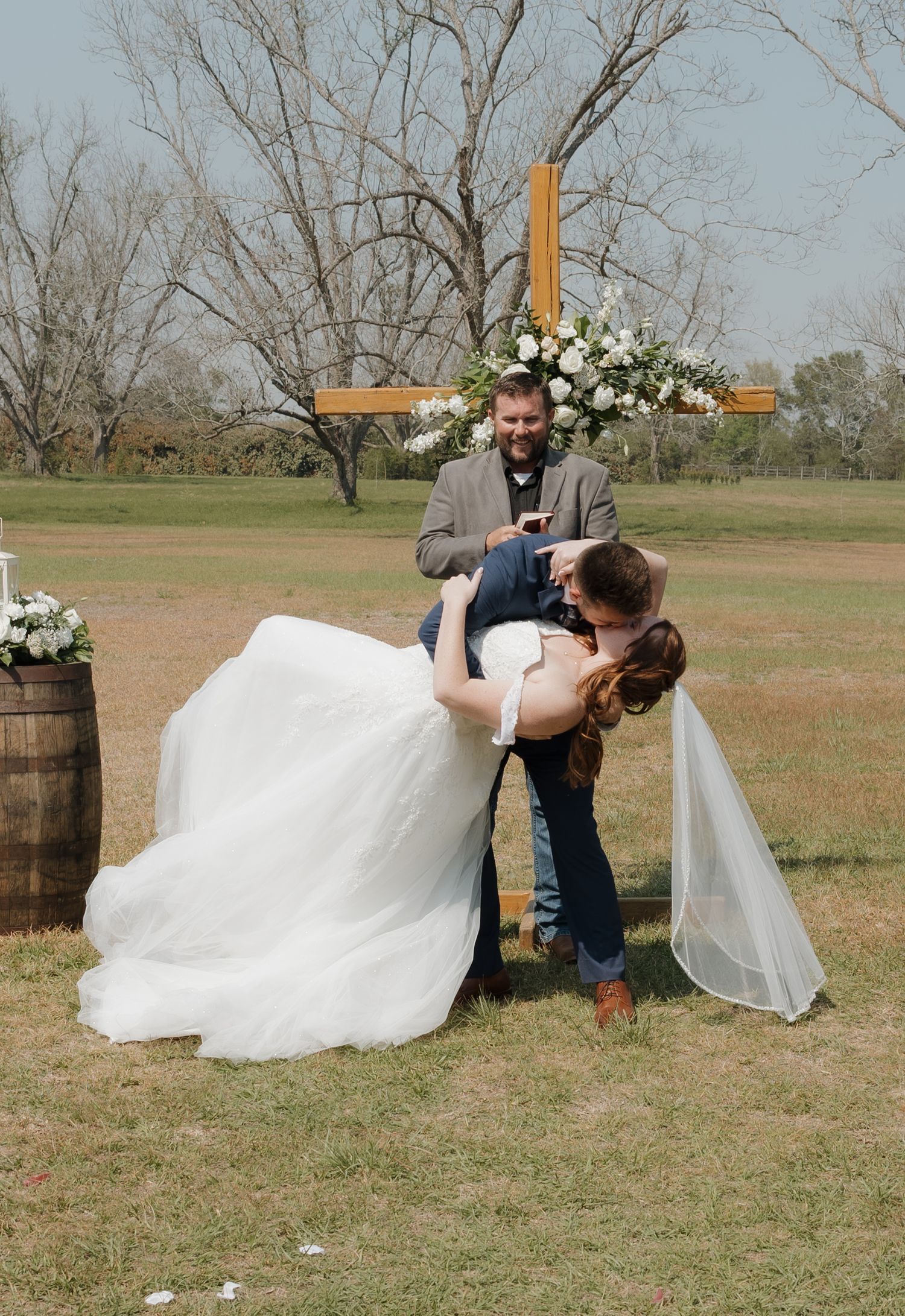 Wedding party posing playfully in outdoor field setting with white dress flowing in the wind.