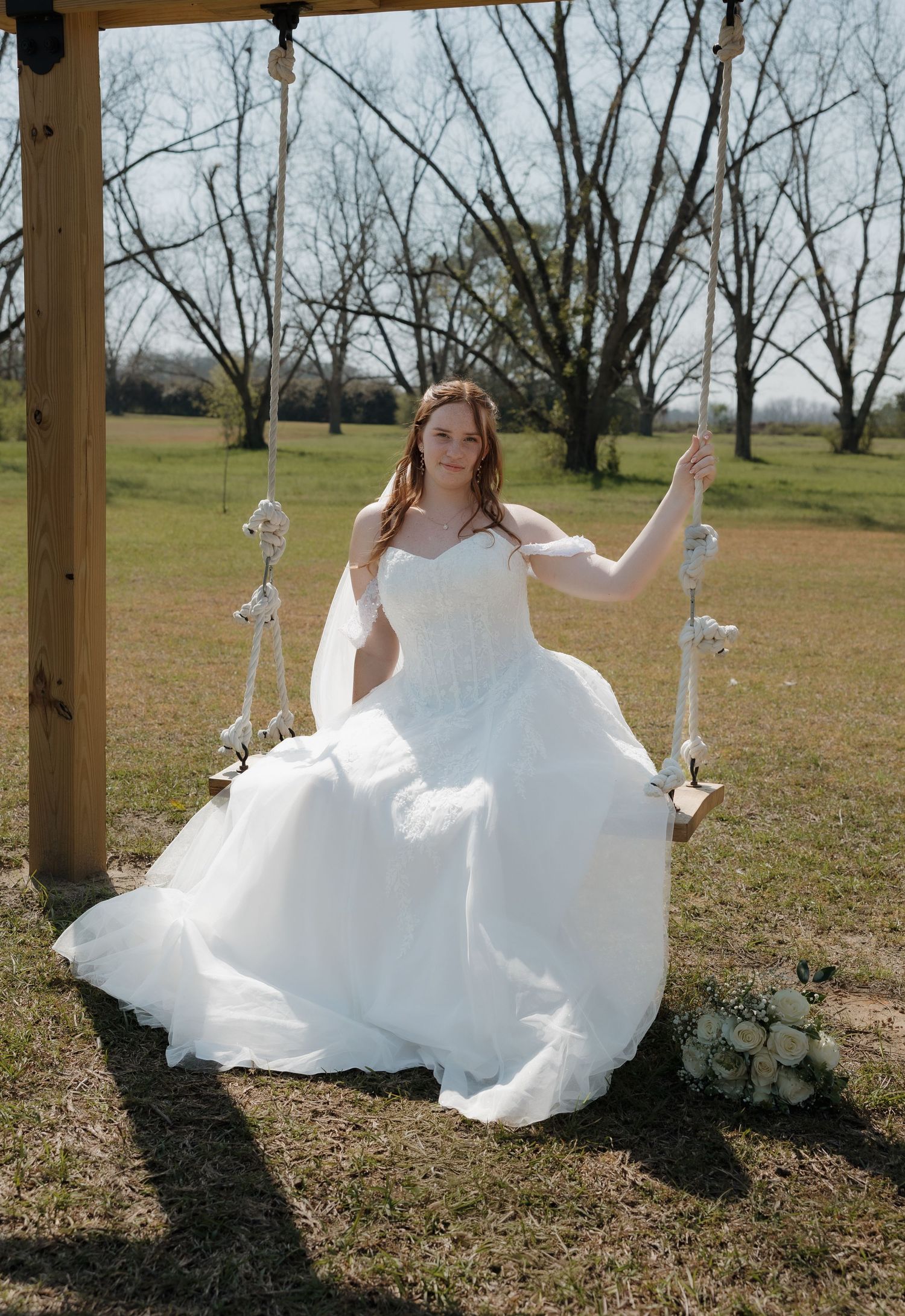 White wedding dress flowing in breeze during outdoor photoshoot under wooden pavilion.