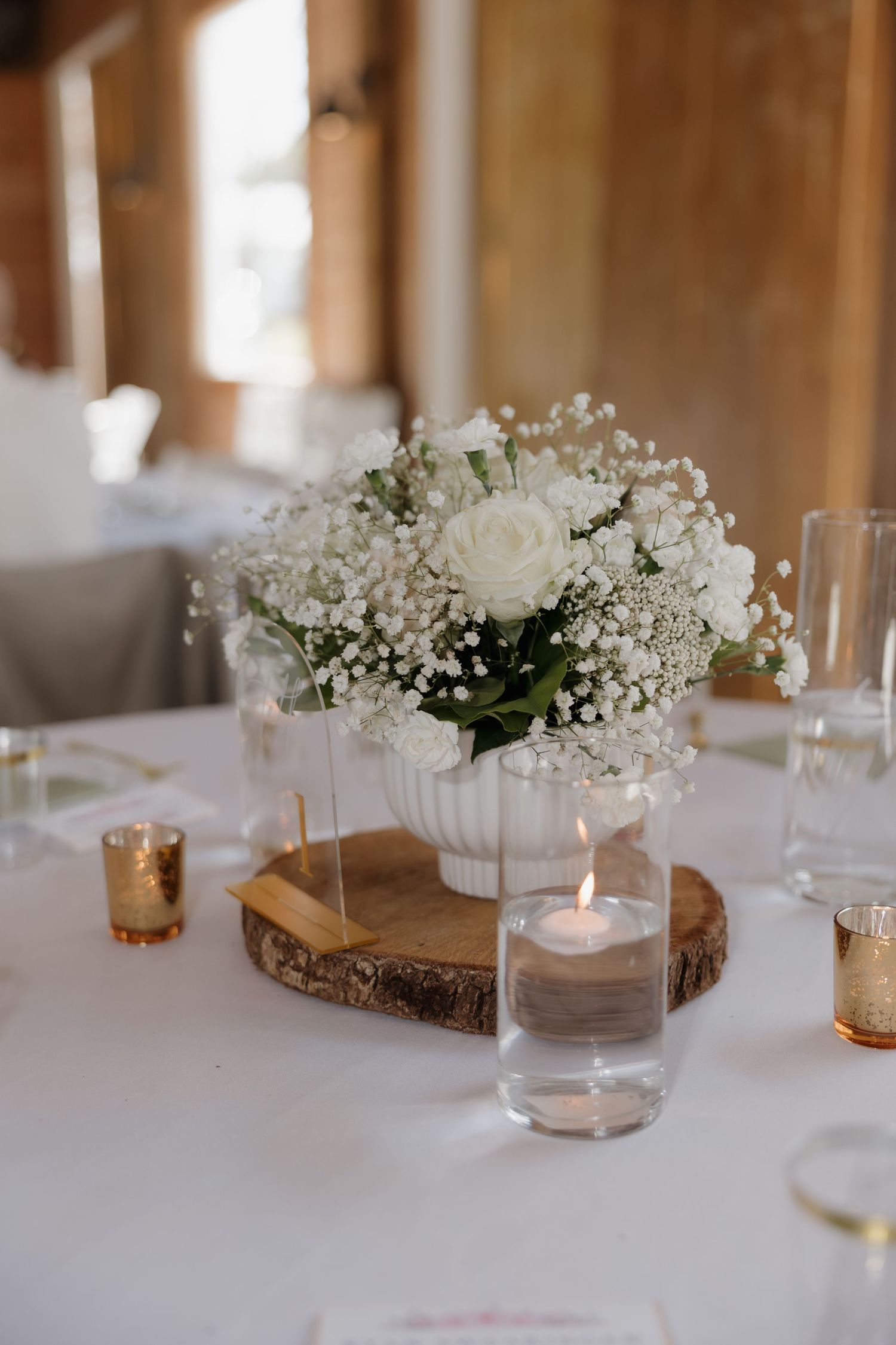 Elegant wedding centerpieces with white flowers on wood slices and glass votives.