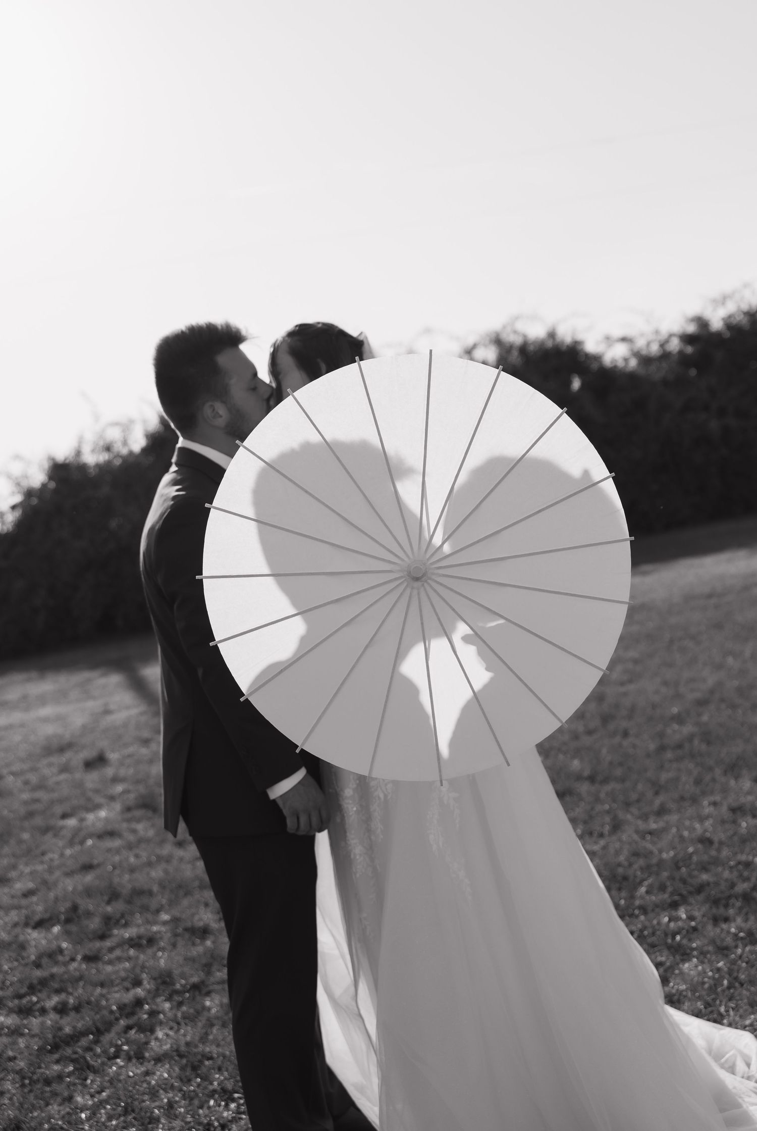 Black and white photos of a couple with a white parasol umbrella in an outdoor setting.