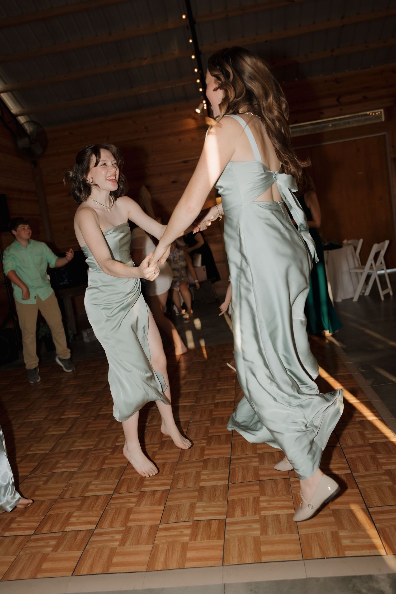 Wedding guests dance energetically on a wooden parquet dance floor at a reception celebration.