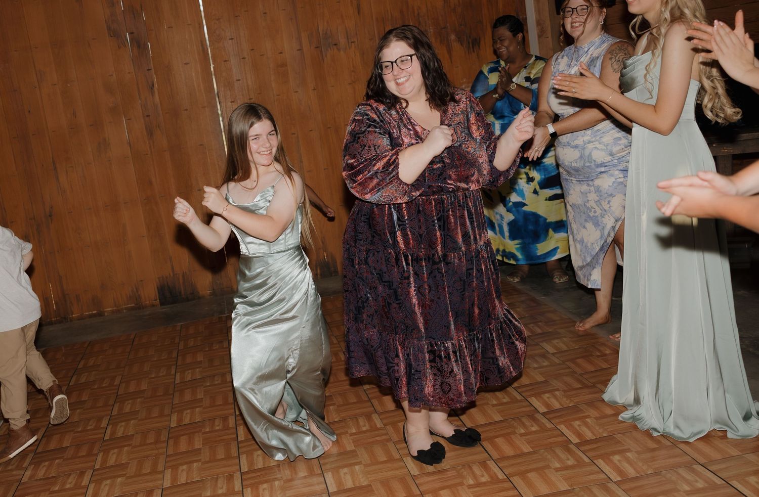 People dancing and celebrating at a wedding reception in a rustic wooden barn venue.