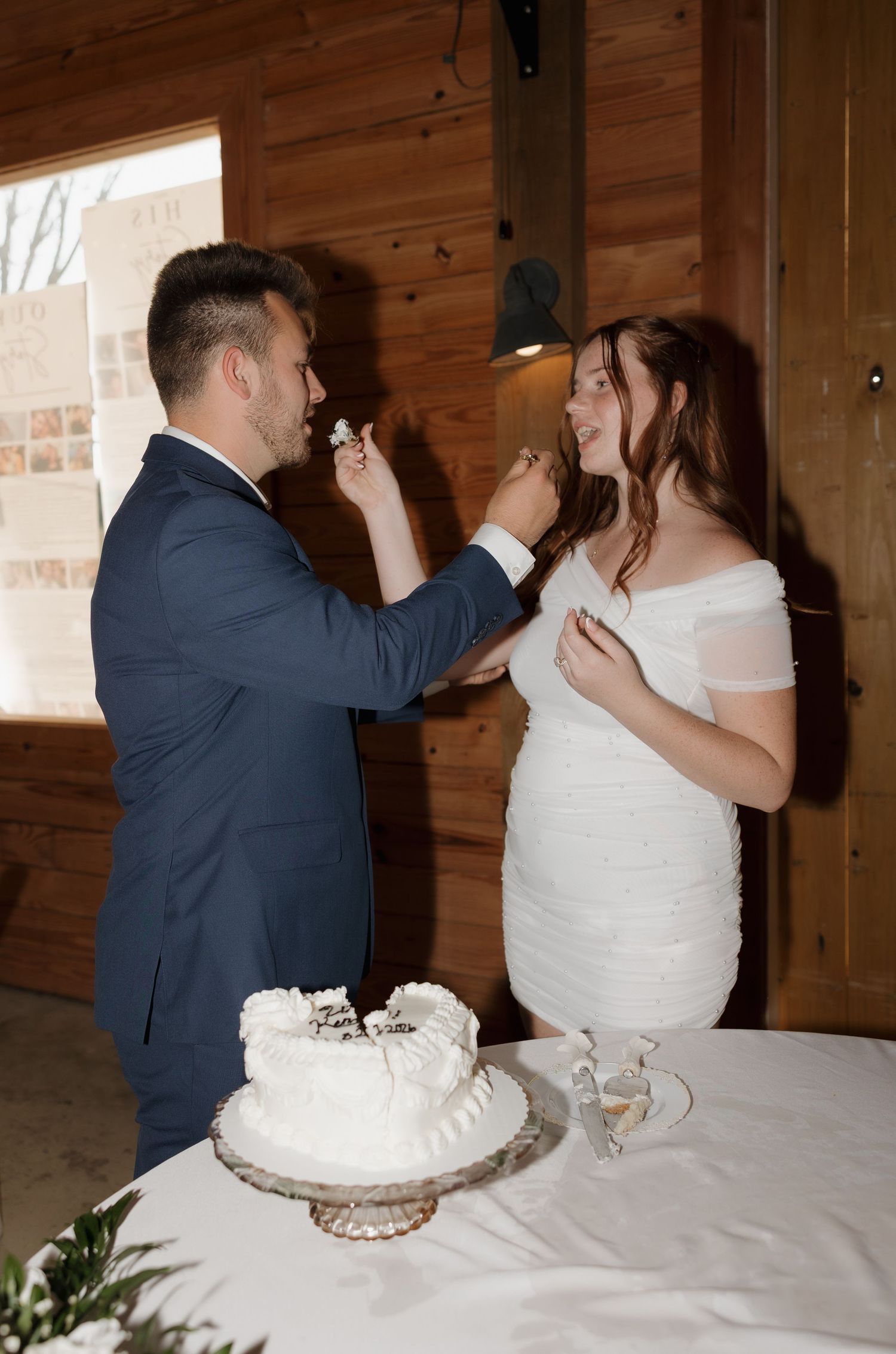 A couple cuts their white wedding cake together at their rustic wooden venue reception.