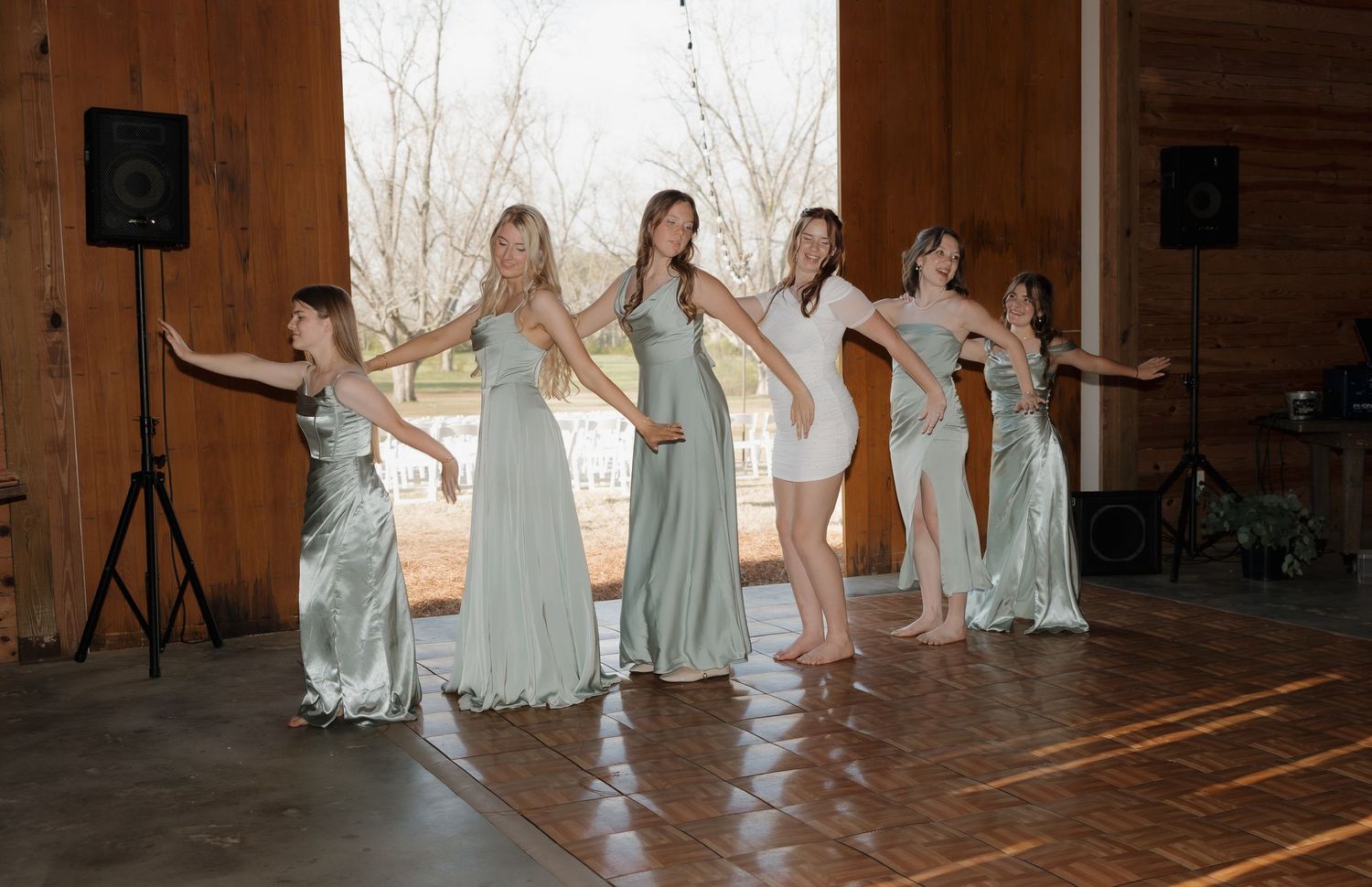 A panoramic view of dancers in flowing white and sage green dresses performing on a wooden stage.