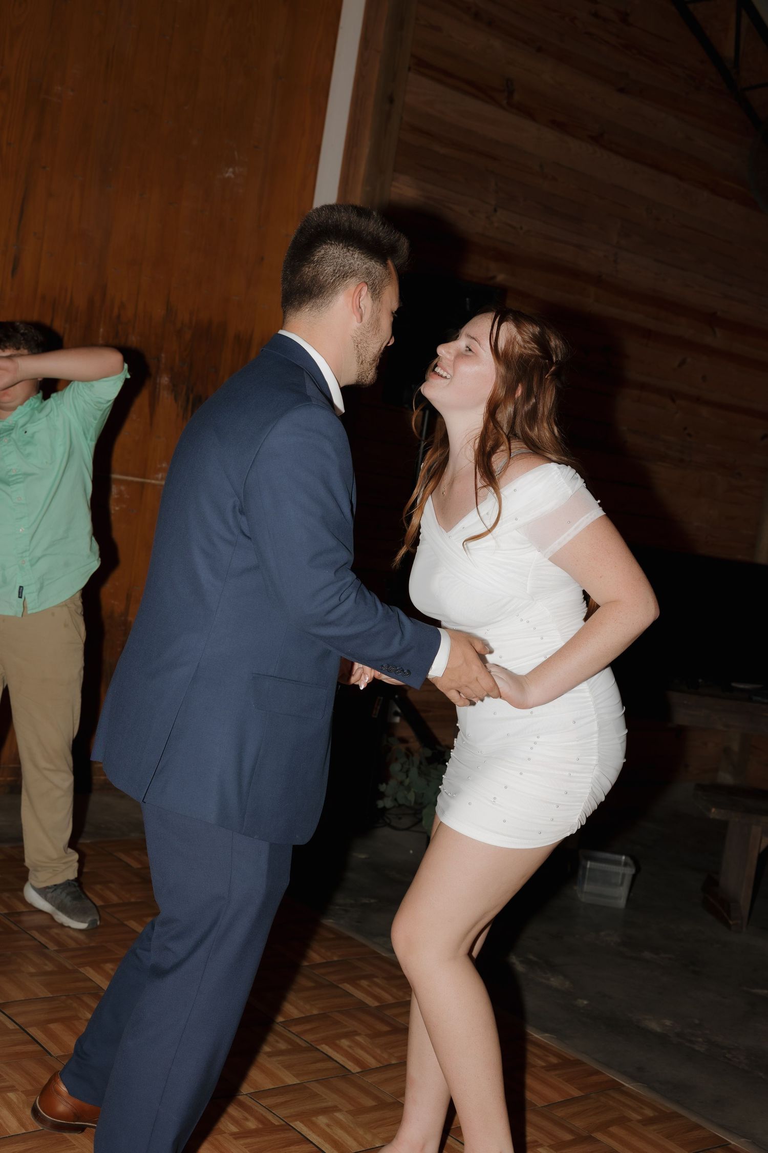 A couple dances energetically at a wedding reception in a rustic venue.