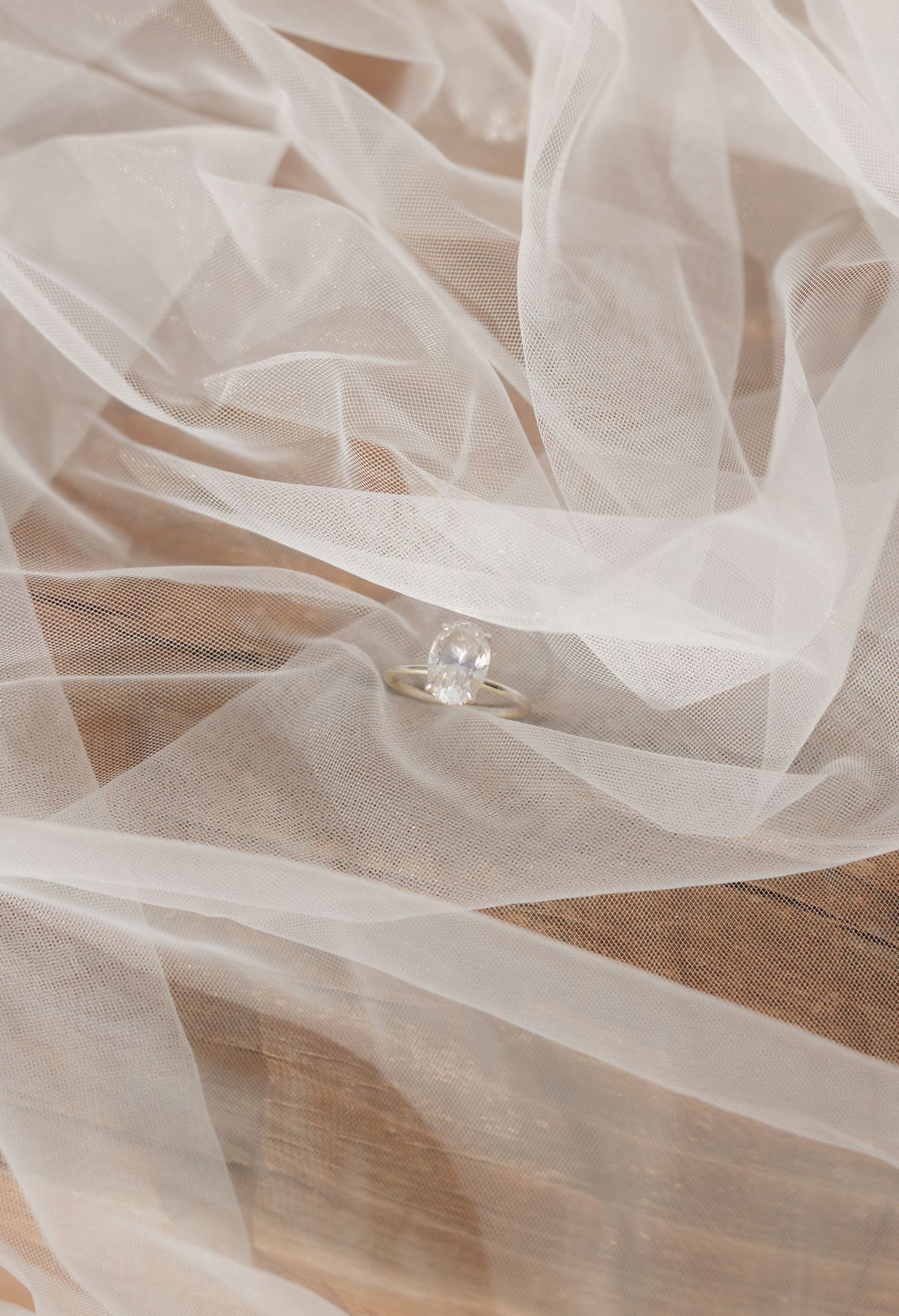 Delicate white wedding veil with lace details laid out on wooden surface.