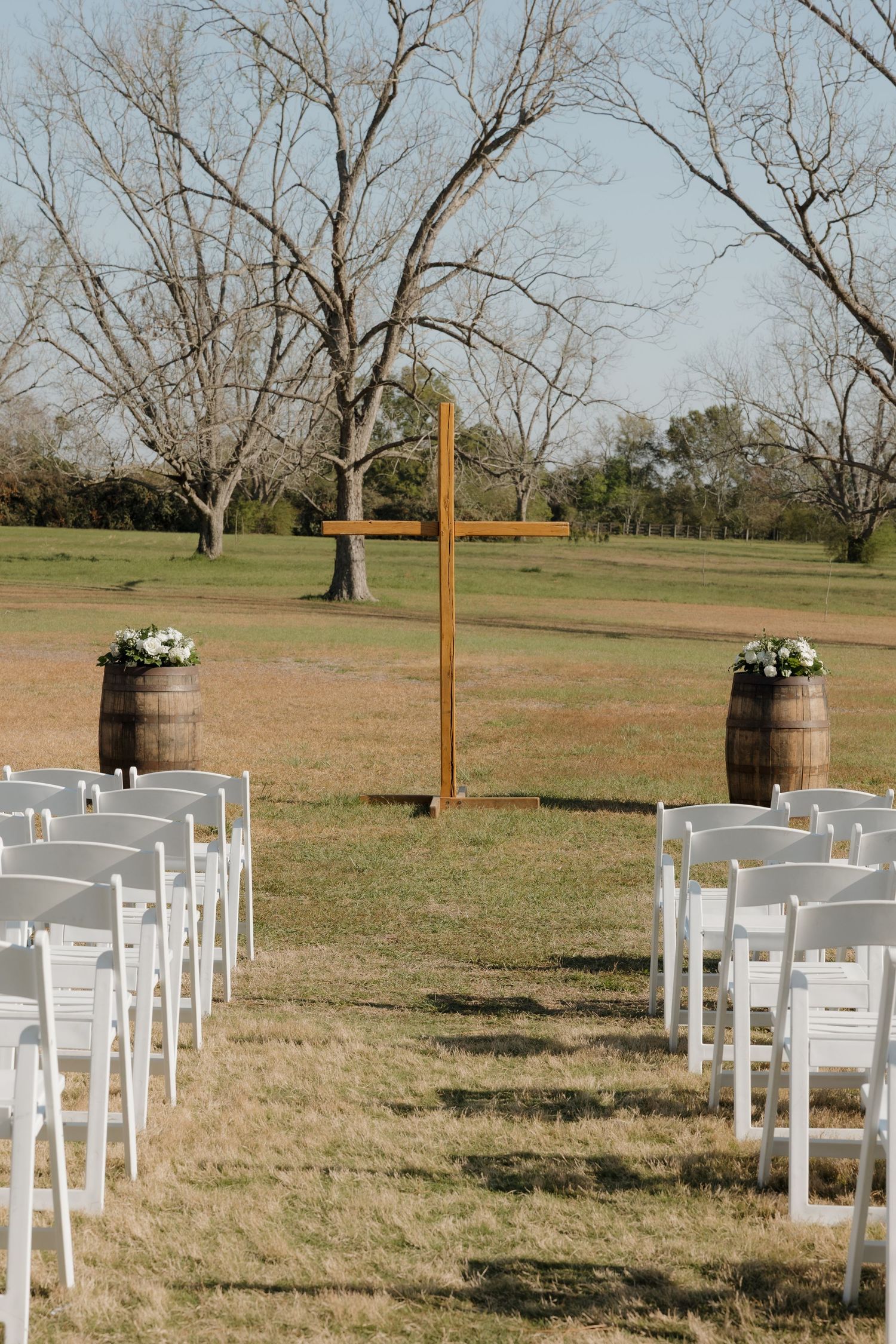 Outdoor wedding ceremony setup with white chairs and wine barrel decor in open field.