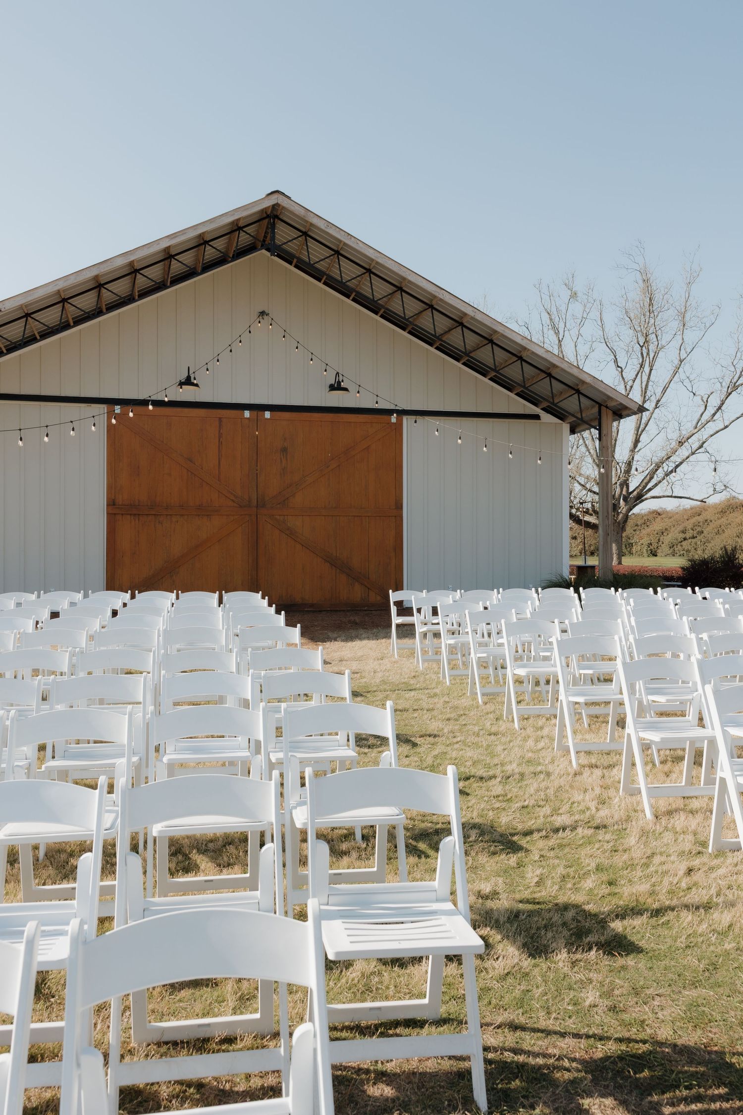 White wooden chairs set up for outdoor wedding ceremony under covered pavilion.