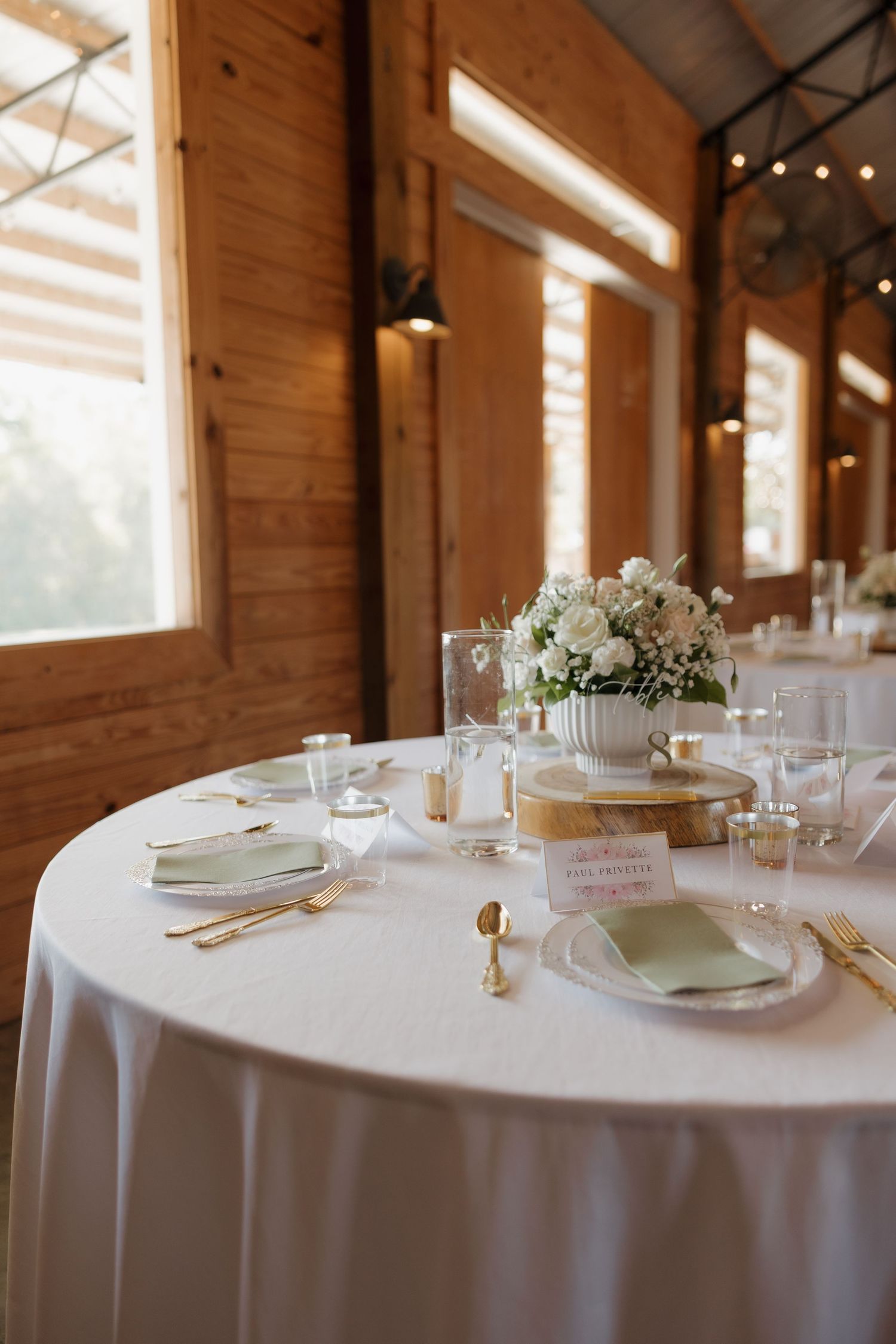 Elegant table settings with white linens and floral centerpieces at a rustic wooden venue.