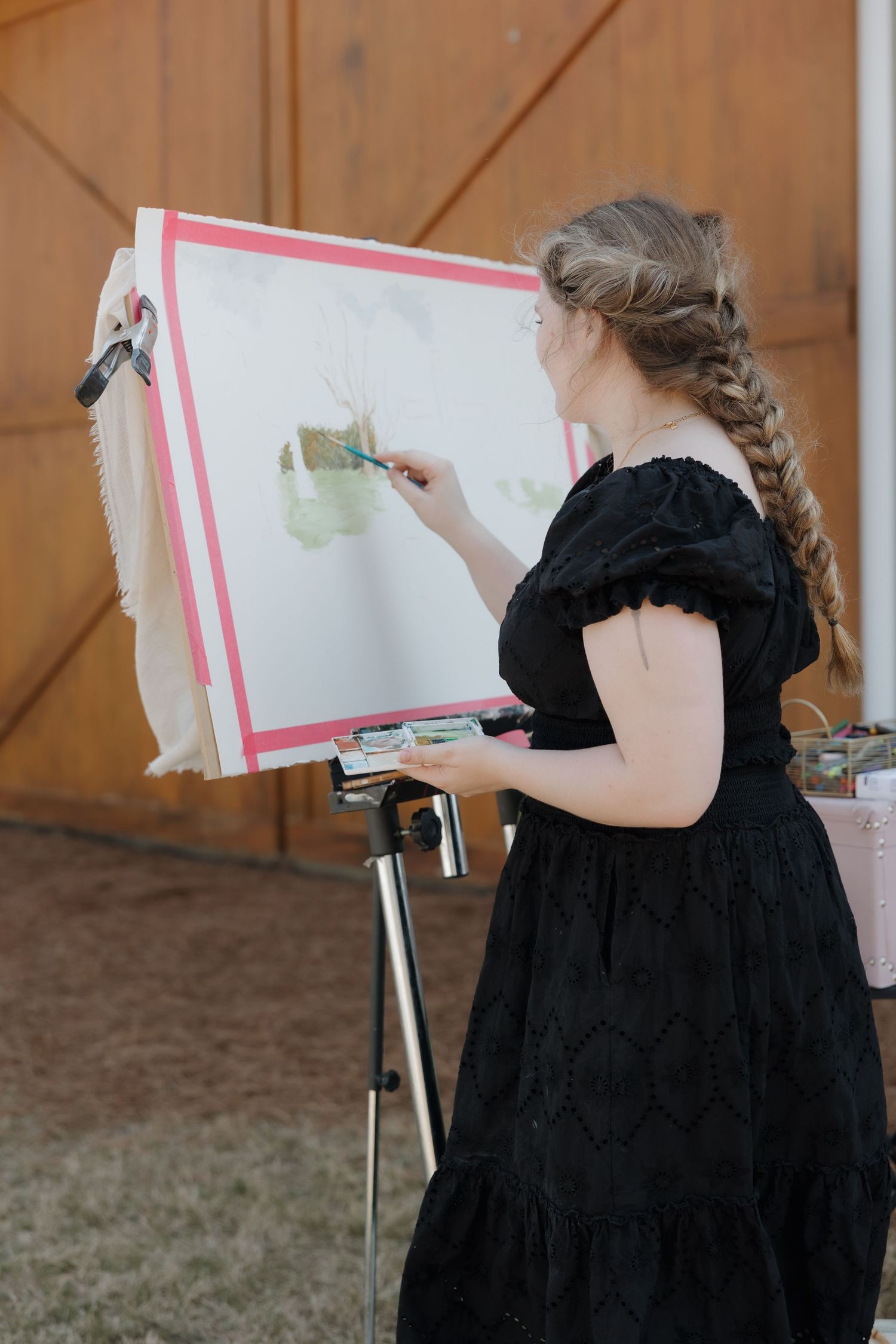 A series of images showing someone in a black dress drawing on an easel outdoors.