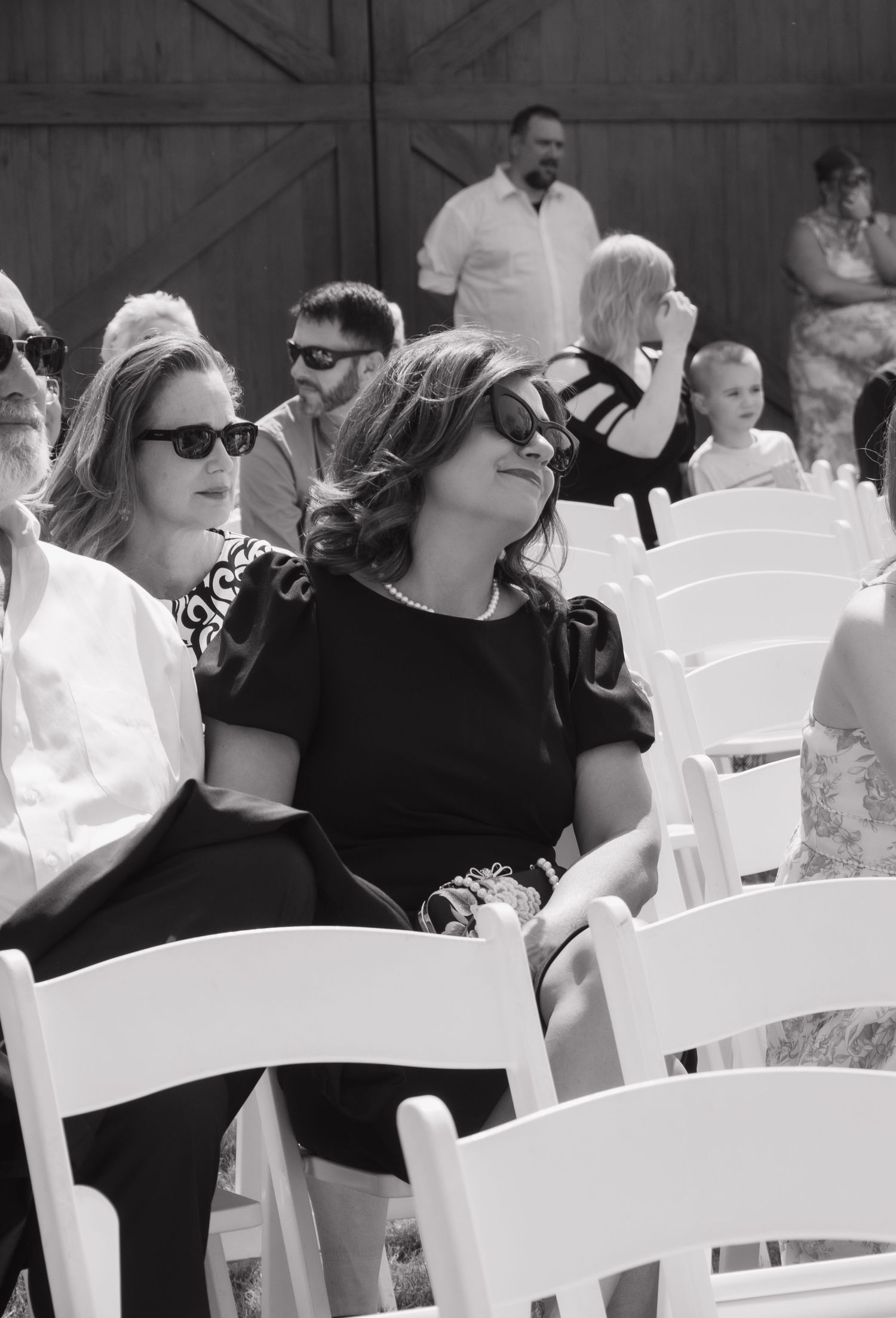 Wedding guests seated in white chairs during an outdoor ceremony.