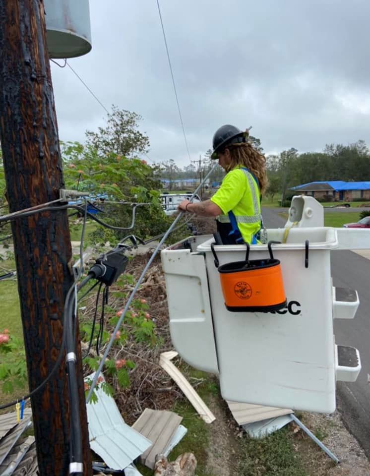 Utility worker in yellow safety vest operates bucket truck repairing power lines after storm damage.