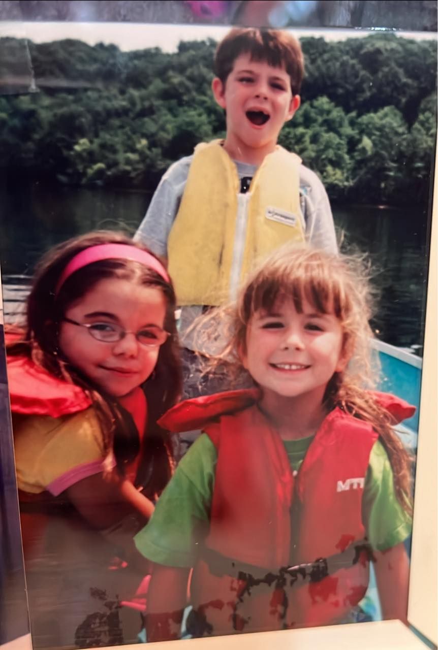 Three happy children wearing colorful life jackets on a boat trip on a scenic river.