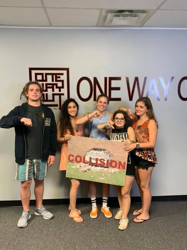 Five young people pose holding a Collision sign at One Way Out escape room.