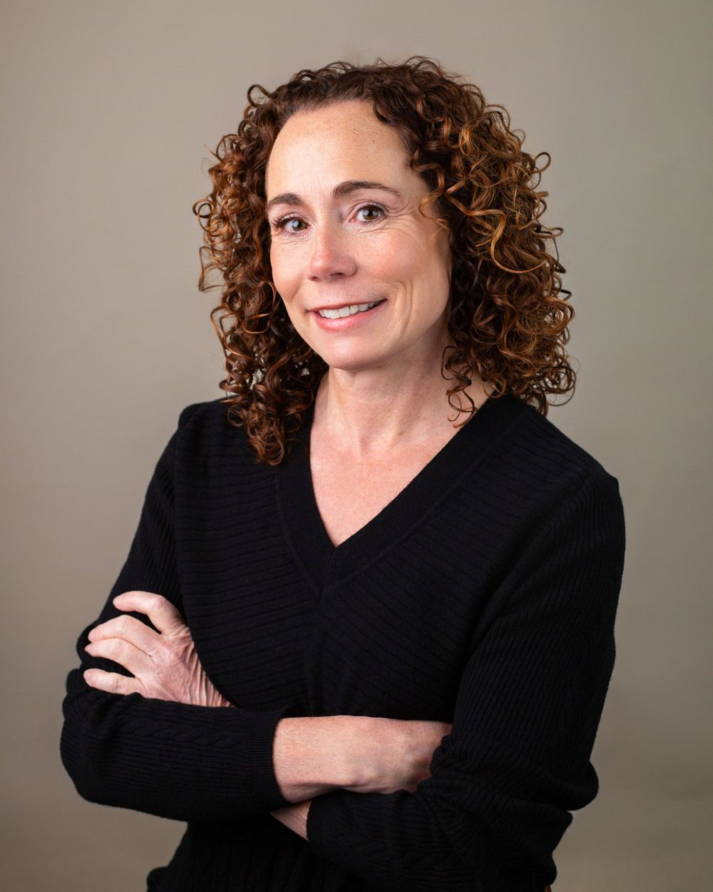 A person with curly red hair wearing a black sweater poses in a series of expressive portraits against a neutral background.