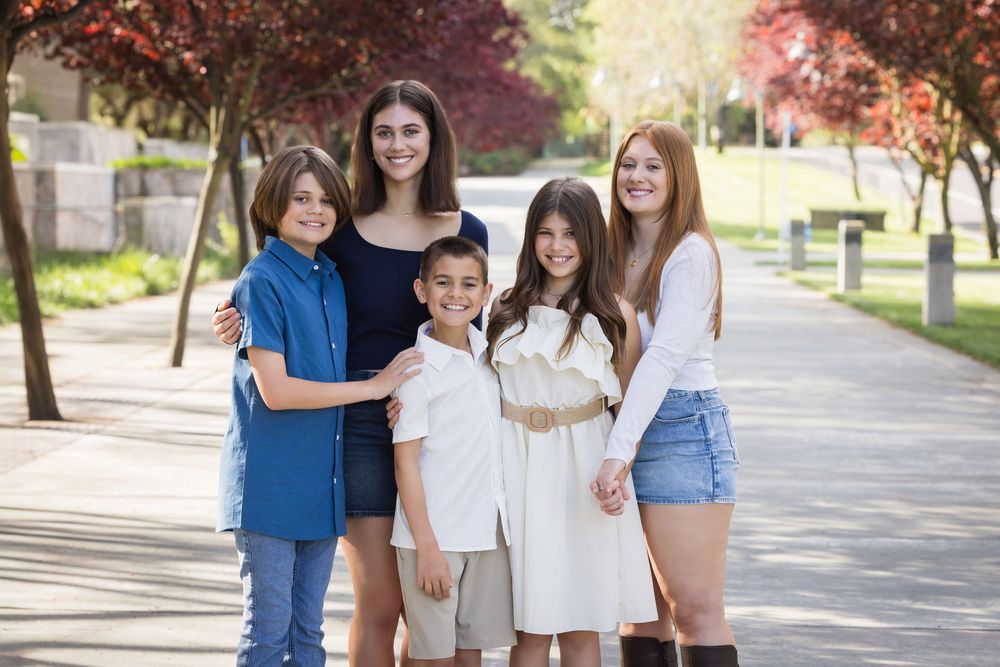 A group of siblings pose together on a tree-lined sidewalk in casual attire during autumn.