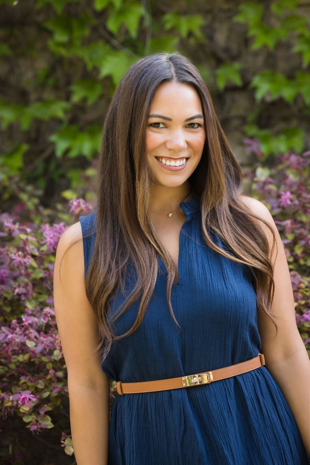Portrait series featuring someone in a navy dress with brown belt against flowering bushes.