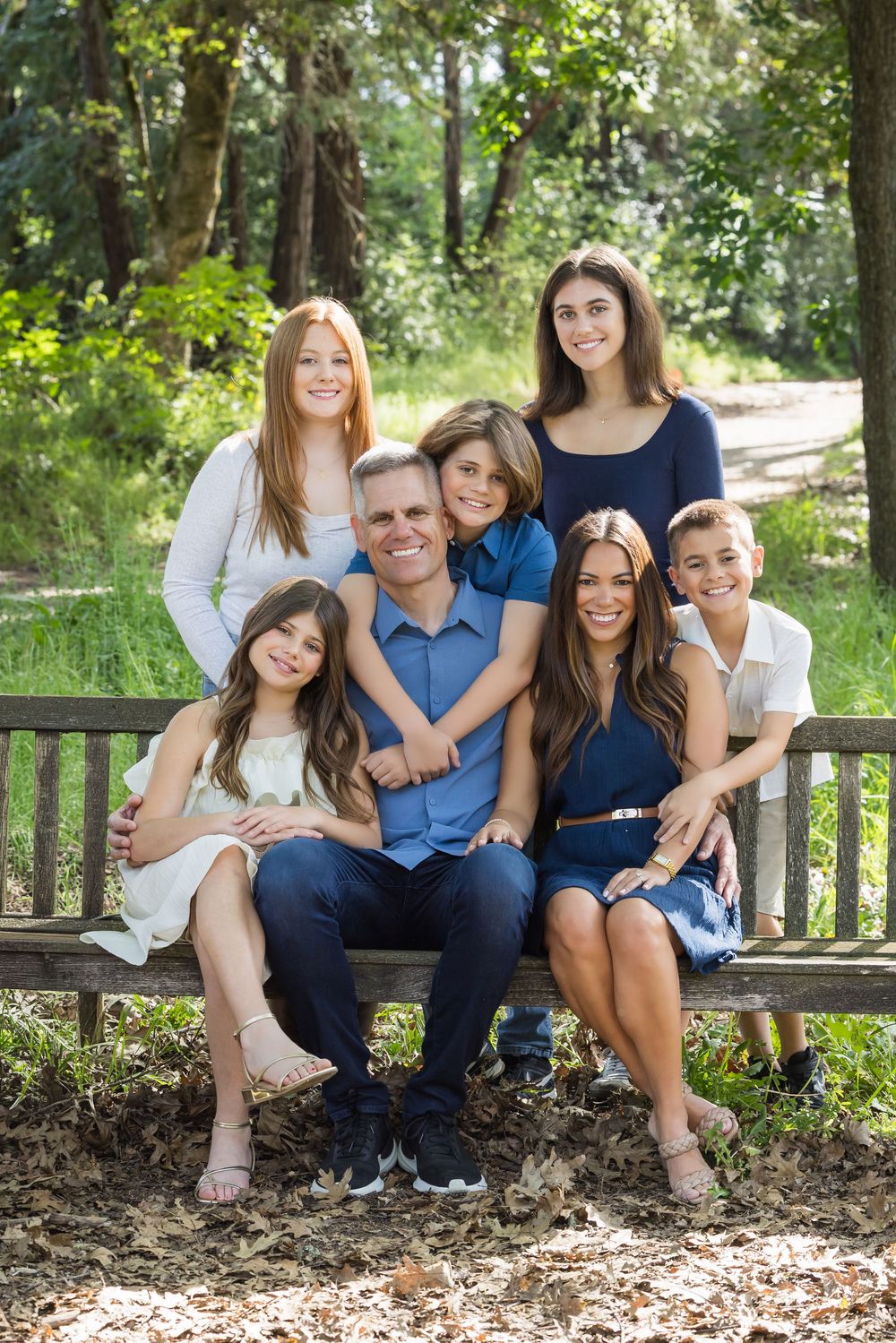 Family group sitting together and smiling on wooden bench in sunny garden setting.