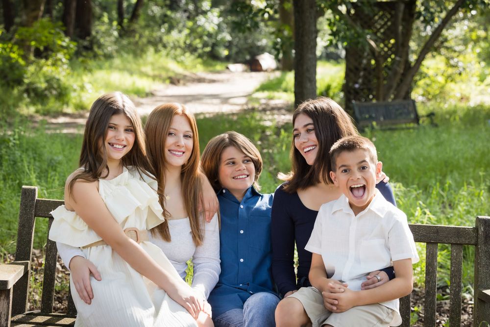 A cheerful group sits together on a wooden bench in a sunny garden setting.