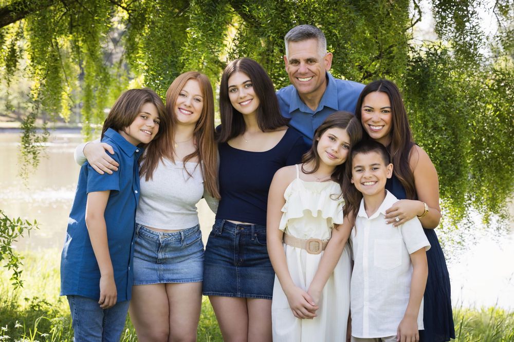 Extended family group photo under a weeping willow tree on a sunny day.