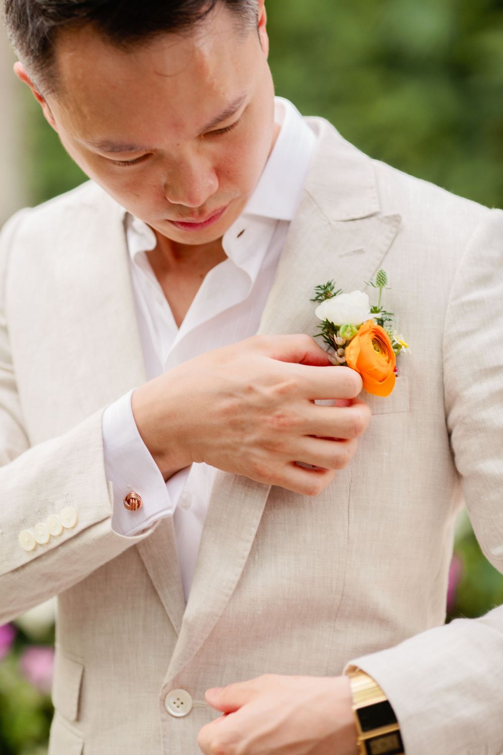 Groom adjusting boutonniere on beige suit jacket during Koh Samui destination wedding preparation.