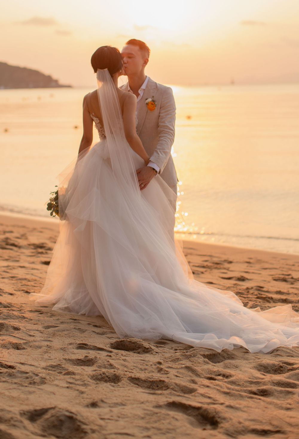 Bride and groom standing together on a sandy beach at sunset, with flowing veil at a Koh Samui destination wedding.