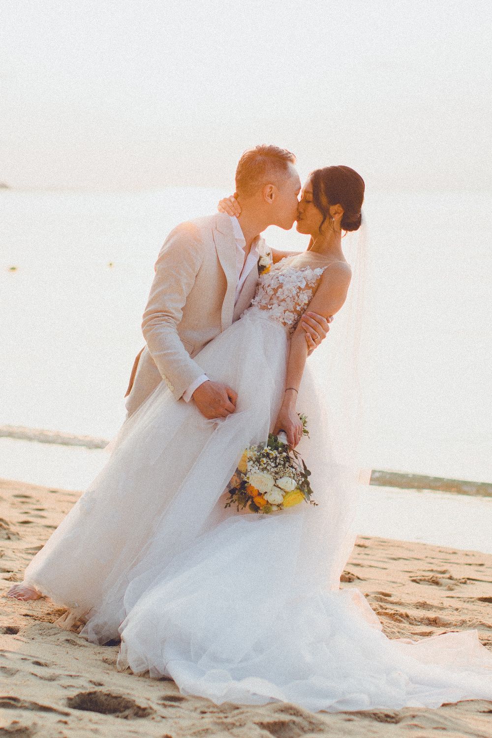 Groom dips and kisses bride on the beach, holding bouquet during a romantic Koh Samui wedding photoshoot
