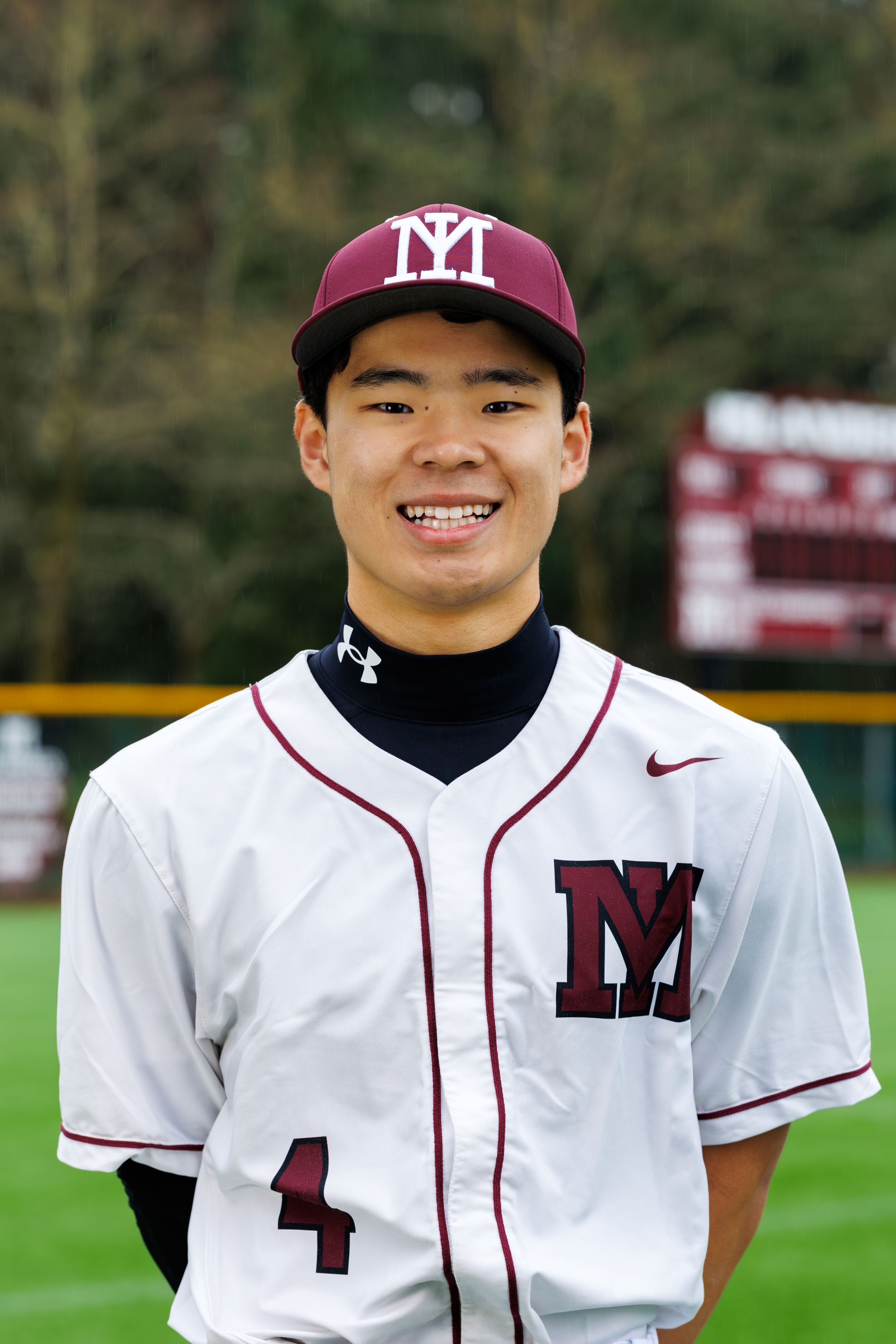 Young baseball player in maroon and white uniform, number 4, smiling on field.