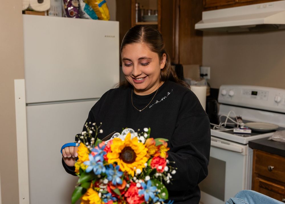 Woman in black sweatshirt smiling while holding a colorful bouquet with sunflowers in a kitchen at the Cottonwood at Platte River State Park