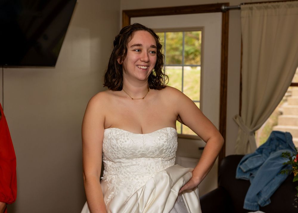 Smiling bride in a strapless white wedding gown getting ready indoors on her wedding day.