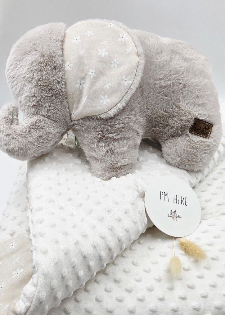 Gray plush elephant stuffed animal resting on white minky dot baby blanket with I'm Here gift tag.